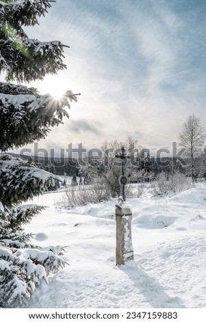 Cross and the winter snowy landscape at Filipova Hut, Sumava national park, sun shining behind the trees