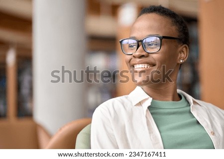 Happy cheerful African teen girl, smiling short-haired cute Black ethnic college student wearing eyeglasses looking away in modern university campus library. Close up portrait. Copy space Royalty-Free Stock Photo #2347167411