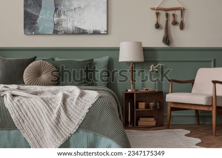 Interior design of cozy bedroom interior with mock up poster frame, bed, sage bedding, beige plaid, lamp, boucle armchair, wooden bedside table and personal accessories. Home decor. Template. Royalty-Free Stock Photo #2347175349
