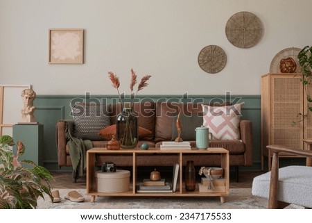 Interior design of cozy living room interior with mock up poster frame, wooden sideboard, brown sofa, wooden partition wall, gray armchair, patterned pillow and  accessories. Home decor. Template.