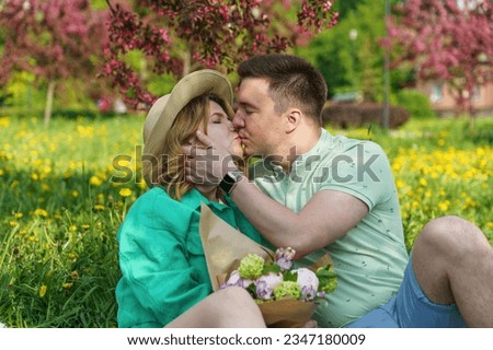 A guy and a girl sit on a picnic blanket in a park, kissing and enjoying their time together. The picture depicts the concepts of weekend, relaxation, dating, and healthy relationship psychology.