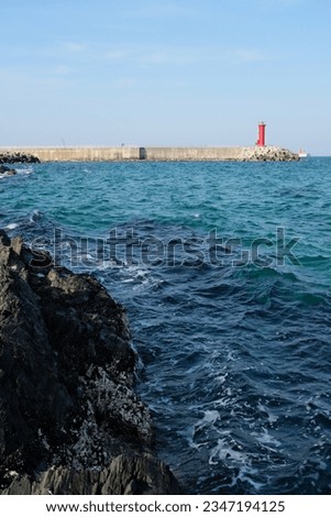 picture of blue sea waves , black sea rocks, red lighthouse and light blue sky Royalty-Free Stock Photo #2347194125