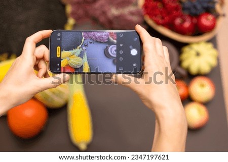 The blogger takes photos and videos on the phone. Hands with phone close-up. A girl shoots a background with an autumn harvest on her phone. Autumn vegetables, fruits, clay brown teapot on a brown