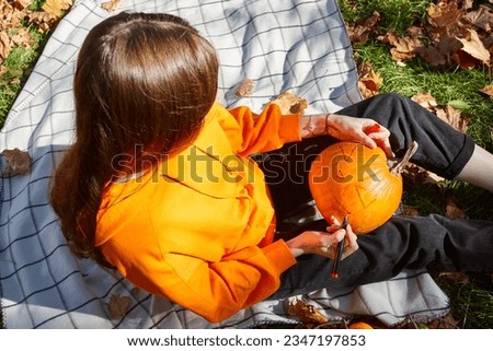 Woman drawing scary face on the pumpkin outdoors in sunny october day
