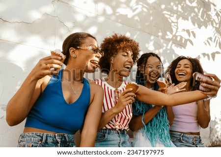 Group of cheery young african american women eating ice cream and taking selfie while spending time together outdoors