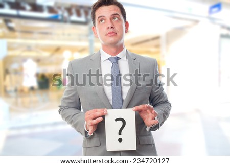 Business man over shopping center background. Holding a card with a question mark