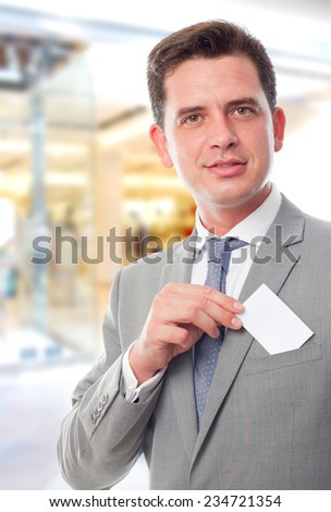 Business man over shopping center background. Showing a business card