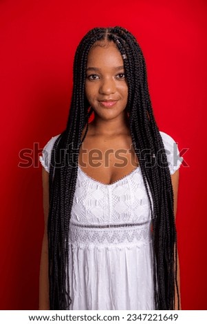 Beautiful young woman with long braids, confident and smiling. Isolated on red background.