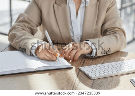 Close up view of millennial woman sit at table hold pencil take notes to paper notebook working studying.