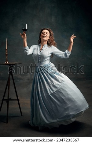 Wine and happiness. Full length ortrait of aristocratic woman wearing blue historical dress and dancing with glass of wine. Concept of healthy lifestyle, diet, style, fashion. Royalty-Free Stock Photo #2347233567