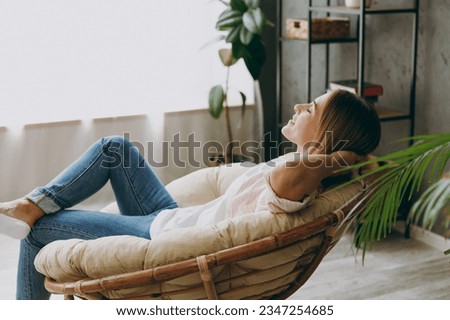 Side profile back view calm blonde young woman wearing casual clothes sit in armchair look camera stay at home hotel flat rest relax spend free spare time in living room indoor. People lounge concept Royalty-Free Stock Photo #2347254685