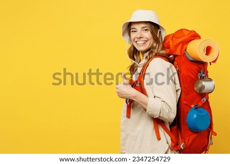 Side view happy young woman carry backpack with stuff mat showing thumb up isolated on plain yellow background. Tourist leads active lifestyle walk on spare time. Hiking trek rest travel trip concept Royalty-Free Stock Photo #2347254729