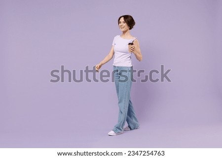Full length side view young smiling fun happy woman 20s wear white t-shirt hold takeaway delivery craft paper brown cup coffee to go walk going isolated on pastel purple background studio portrait.