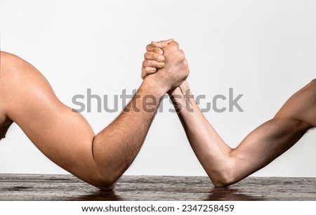 Heavily muscled man arm wrestling a puny weak man. Two man's hands clasped arm wrestling, strong and weak, unequal match.