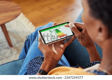 Close up of african american woman holding smartphone with energy efficiency chart and class on screen. Black female hands holding smart phone and looking at house efficiency rating. Royalty-Free Stock Photo #2347259377