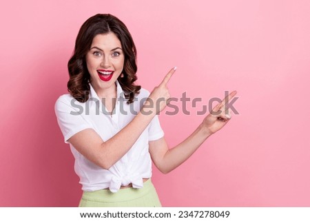Photo of positive excited woman dressed white shirt pointing two fingers empty space smiling isolated pink color background