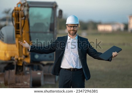 Construction manager in suit and helmet at a construction site. Construction manager worker or supervisor wearing hardhat in front of house. Supervisor construction manager near excavator. Renovation.