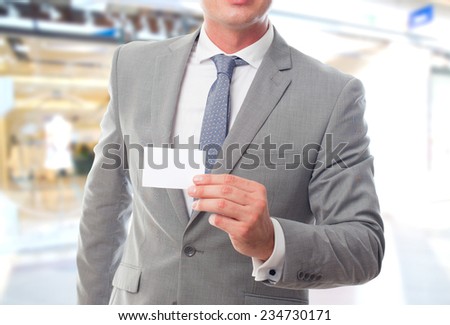 Business man over shopping center background. Showing a white card