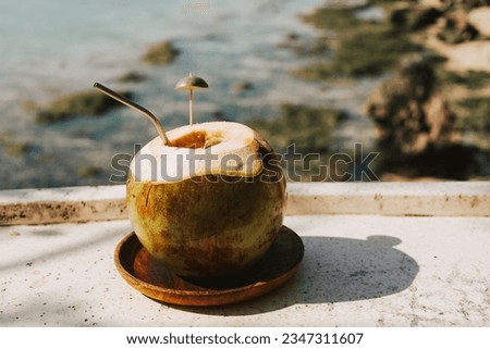 Large green coconut with straw and lime on a wooden stand against the background of the ocean