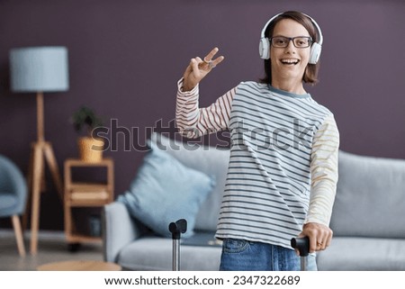 Waist up portrait of smiling teenage girl with cerebral palsy wearing headphones and posing at home showing peace sign, copy space Royalty-Free Stock Photo #2347322689