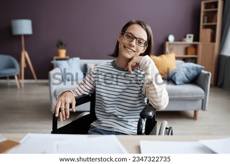 Front view portrait of smiling teen girl with disability looking at camera at desk in home interior, copy space Royalty-Free Stock Photo #2347322735