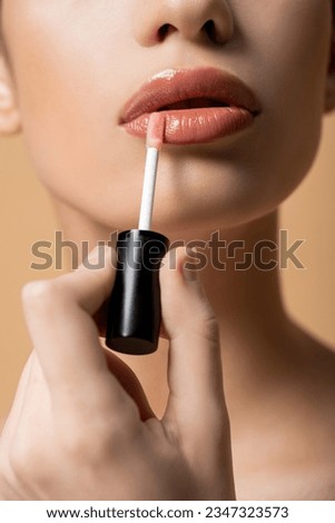 Cropped view of young woman applying lip gloss while doing makeup isolated on beige Royalty-Free Stock Photo #2347323573