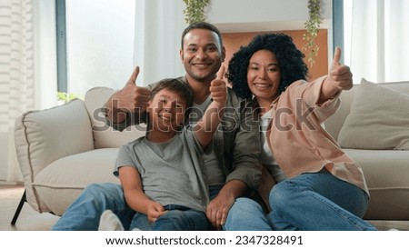 Happy multiracial family African American parents embrace with Caucasian little boy son adopted kid on home floor talk laugh fun weekend smiling father mother and cute child showing thumbs up gesture Royalty-Free Stock Photo #2347328491