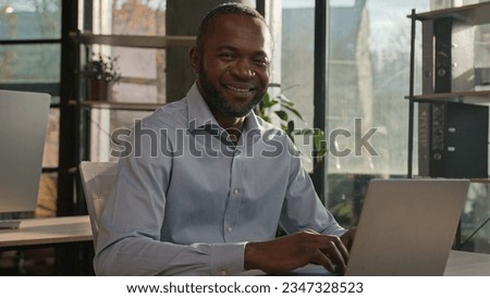 Middle-aged mature African American ethnic man worker CEO director sit at sunny office business agency company typing email on laptop computer search data online networking businessman smiling smile