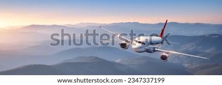 Plane is flying in colorful sky at sunset. Landscape with passenger airplane over mountains ranges and hills in fog, orange sky. Aircraft is landing. Business. Aerial view. Transport. Private Jet Royalty-Free Stock Photo #2347337199