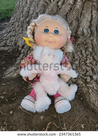 A little girl doll and her teddy bear relaxing next to a tree