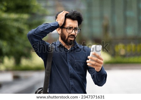 Upset sad young eastern businessman reading bad news online using app on phone, thinking man outside office building disappointed with achievement results at workplace, boss depressed, touching head Royalty-Free Stock Photo #2347371631