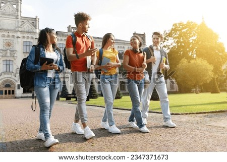 Five multiethnic students chatting and laughing while walking together at university campus, group of happy young people with books and backpacks going to classes or having fun after lessons Royalty-Free Stock Photo #2347371673