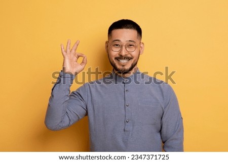 Happy Young Asian Man Showing Ok Gesture At Camera, Cheerful Millennial Guy In Eyeglasses Gesturing Sign Of Approval, Saying I'm Fine While Standing Over Yellow Studio Background, Copy Space