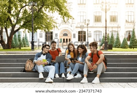 Group Of Students With Digital Tablet And Laptop Study Together Outdoors, Happy Multiethnic Young Friends Sitting On Stairs Near University Building, Using Modern Gadgets For Education, Copy Space Royalty-Free Stock Photo #2347371743