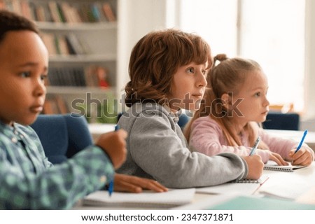 Elementary classroom of diverse children listening attentively to their teacher giving lesson, kids in school writing in exercise notebooks or taking a test Royalty-Free Stock Photo #2347371871