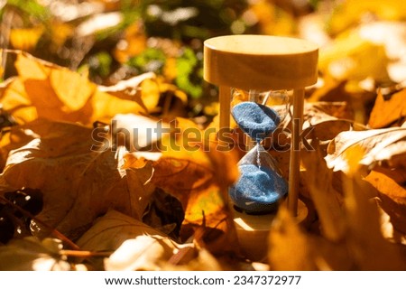 Hourglass and autumn leaves in the park. A symbol of passing time. Symbol of short life. Royalty-Free Stock Photo #2347372977