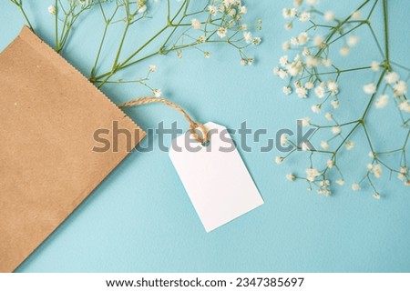 A mock-up of a white tag, a label and a price tag near a craft bag with flowers lie on a blue table. Empty space for text. Close-up