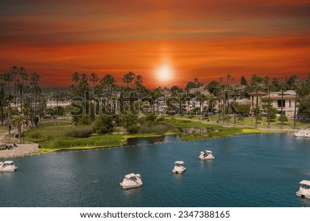 aerial shot of a people in pedal boats on the green waters of Echo Park Lake with lush green trees and plants and people walking through the park at sunset in Los Angeles California
