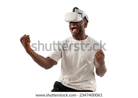 african american male winner in white t-shirt plays and wins in virtual reality glasses on white isolated background, the guy uses modern vr gadget and rejoices in victory and success