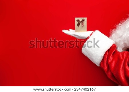 small gift box in the hands of santa claus on red background, santa gives festive gift for the new year, close-up