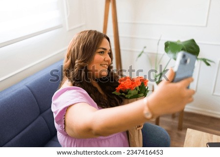 Attractive hispanic woman smiling receiving flowers from her long-distance boyfriend and taking a selfie with her smartphone for social media