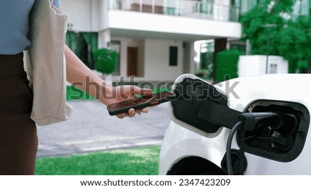Progressive lifestyle of a modern woman who have just returned from work in an electric vehicle that is being charged at home. Electric vehicle powered by sustainable clean energy.
