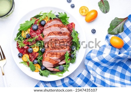 Gourmet salad with grilled duck breast and red orange, kumquat, blueberry, swiss chard, lettuce and arugula on white table background, top view
