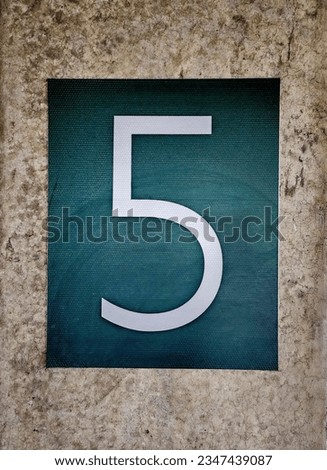 Number 5 sign in white printed on dark green vinyl sign background stuck on old cement wall. The number 5 sign is mounted on the wall to indicate the parking floor, meeting point, location, etc.