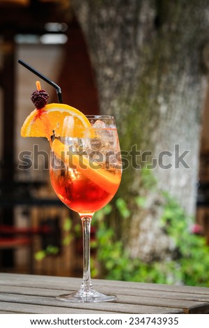 orange cocktail drink in front of a green tree on a garden table