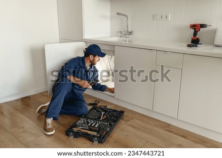 Professional plumber in blue uniform fixing broken water tap in kitchen. Repair service concept Royalty-Free Stock Photo #2347443721