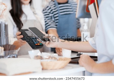 Female customer holding phone near nfc terminal make contactless mobile payment with waitress barista saleswoman on coffeeshop counter, woman client pay in cafe with cellphone via pos machine.
