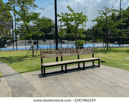 wooden chairs in the park with a basketball court and clear blue sky in the background