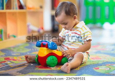 Adorable Asian baby boy in kindergarten or daycare. Child playing with colorful educational toys in preschool. Kids play in indoor playground. Early education and child care.