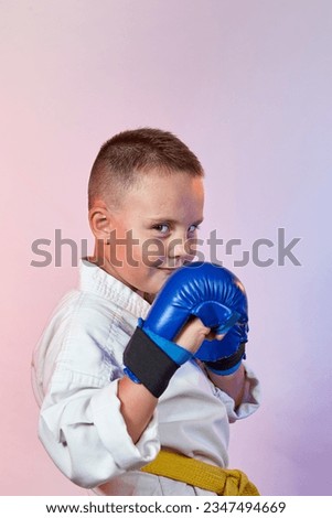 On a gradient colored background, a small athlete in karategi and with blue overlays on his hands Royalty-Free Stock Photo #2347494669